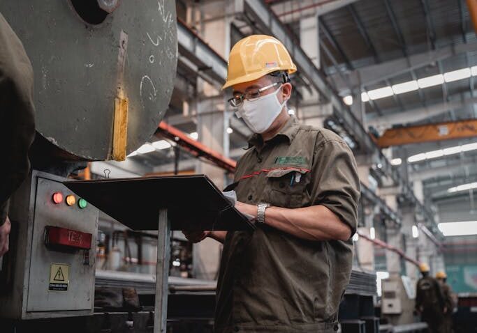 Factory worker with safety gear checks machinery, ensuring industrial safety compliance.