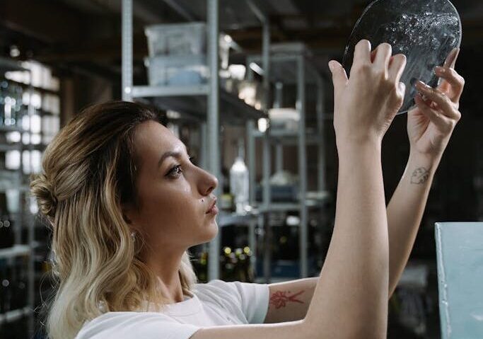A woman carefully examines a metal disc in an industrial workshop setting.